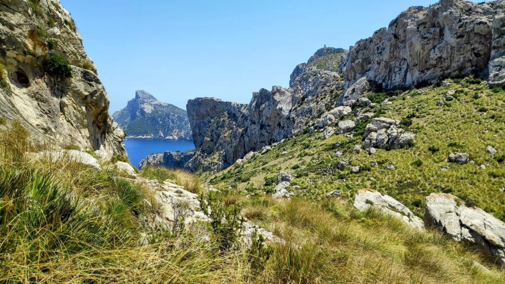 Vista panorámica del valle entre montañas en la Sierra de Albercutx, con vegetación y mar visible al fondo.