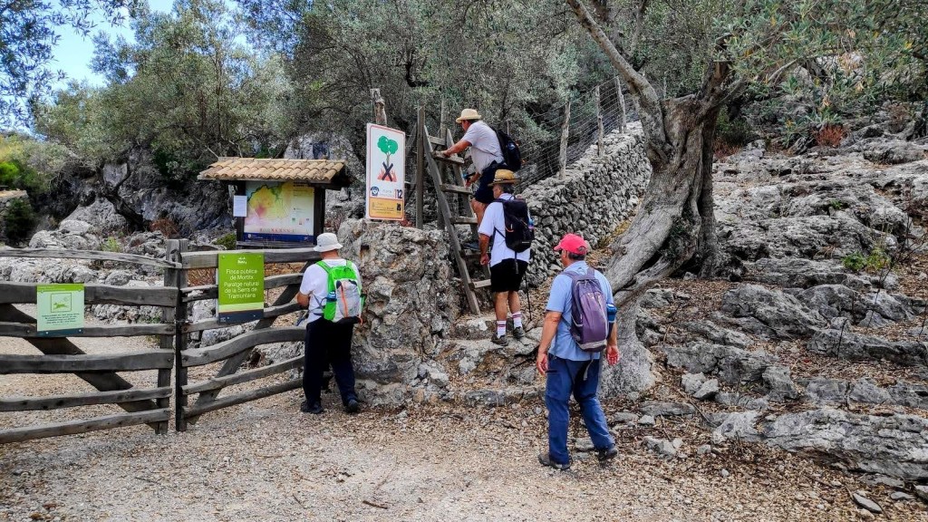 Grupo de excursionistas comenzando la ruta en la finca de Mortitx, pasando por una barrera de madera en un entorno rocoso y natural.