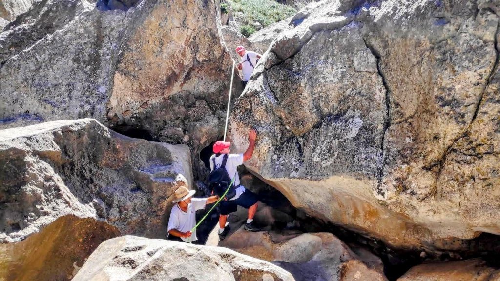 Grupo de personas utilizando cuerdas para escalar entre grandes rocas en la ruta Torrent de Pareis, en la Serra de la Tramuntana.