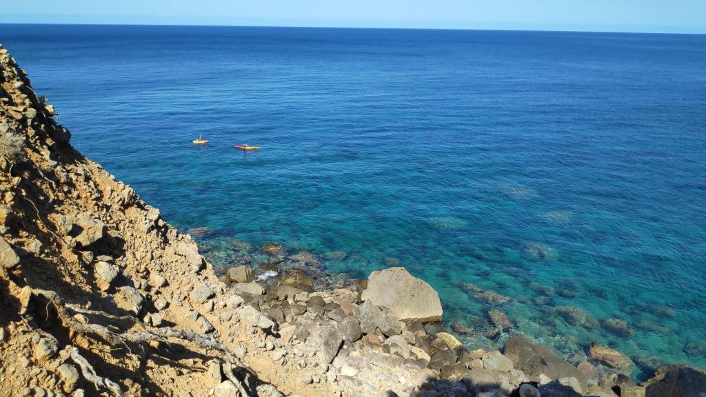 Vista desde un acantilado sobre el mar, con dos kayaks amarillos en las aguas cristalinas.