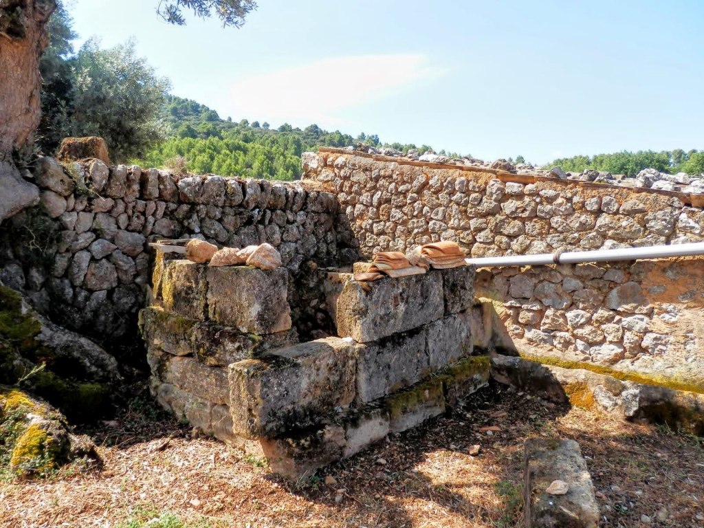 Vista de un antiguo aljibe de piedra en un entorno natural con paredes de piedra, tapizado de vegetación alrededor.