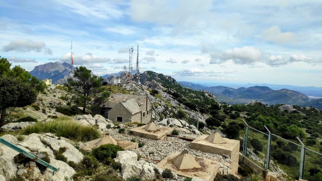 Vista panorámica desde el Puig d'Alfàbia, con antenas visibles en la cima y un paisaje montañoso de fondo.