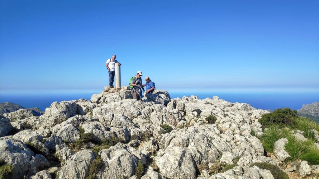 Grupo de personas en la cima del Puig Tomir, rodeadas de rocas y paisaje montañoso bajo un cielo azul claro.