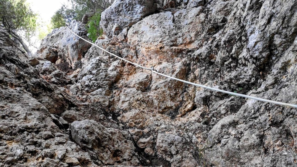 Vista del Pas de Can Boqueta en la Ruta del Puig de Sa Galera, mostrando un tramo rocoso con una cuerda de seguridad en un sendero estrecho.