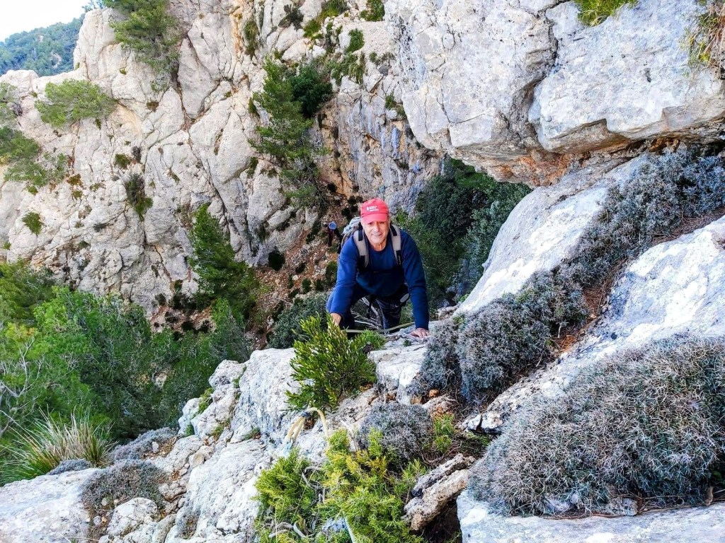 Una persona escalando el Pas d’en Marc, rodeada de vegetación y con una pendiente pronunciada al fondo.
