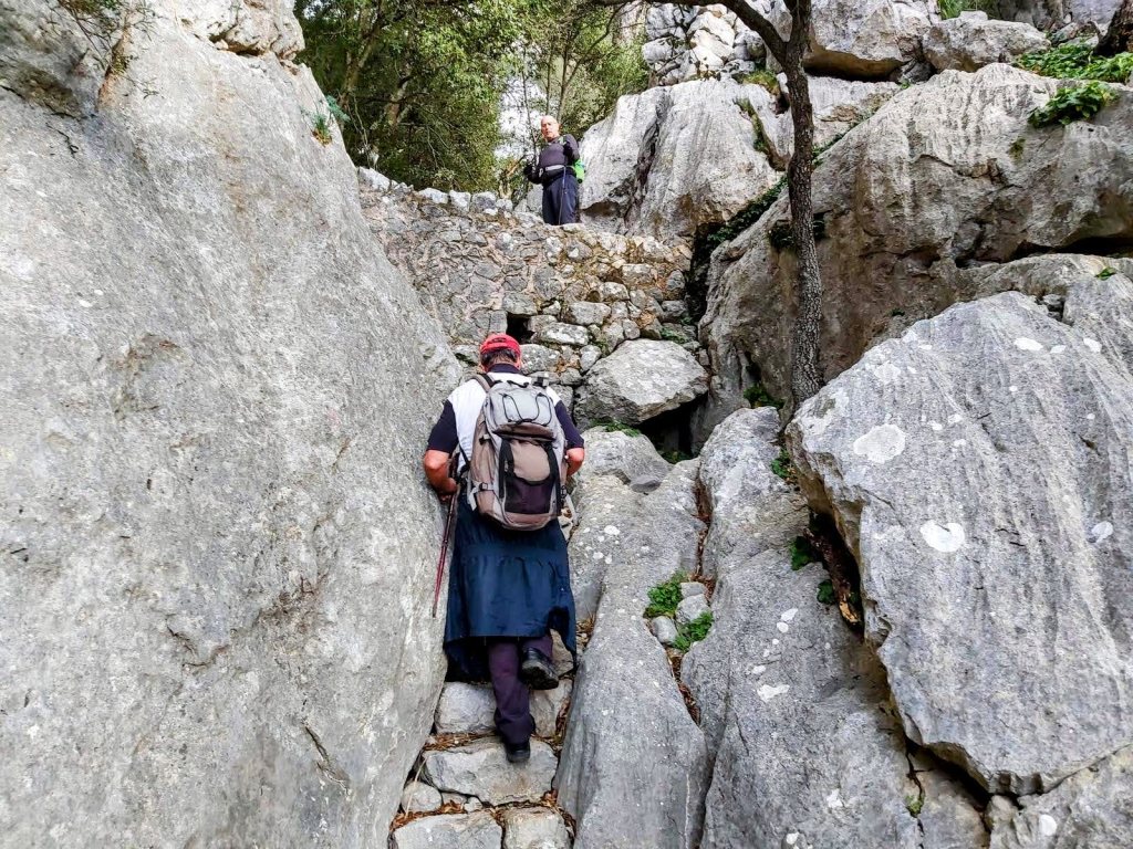 Sendero rocoso en la Ruta Castillo de Alaró, con excursionistas ascendiendo por escalones del Pas de s’Escaleta.