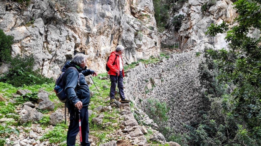 Dos senderistas en la ruta del Puig de Garrafa, observando una estructura de piedra en un entorno montañoso.