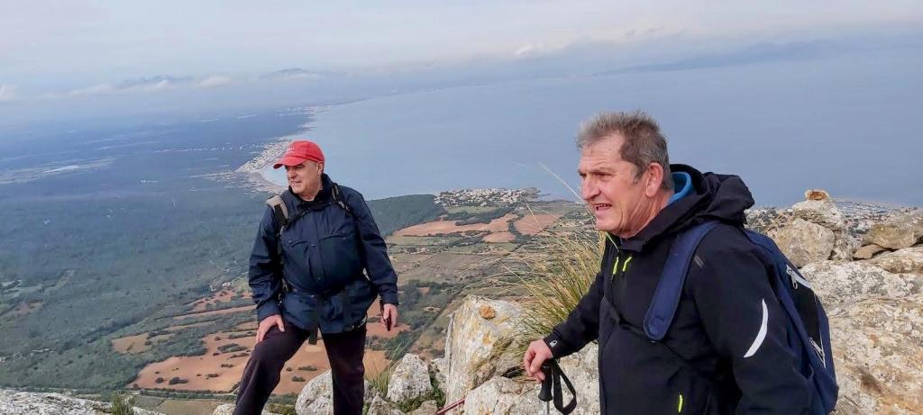 Dos hombres en la cima del Bec de Ferrutx, rodeados de un paisaje montañoso que muestra vistas panorámicas del valle y la costa.