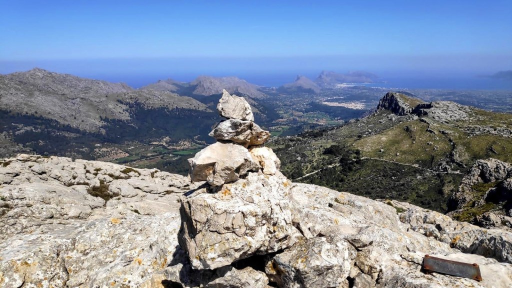 Vista panorámica desde la cima del Puig de Ca Miner, con un hito de piedras en primer plano y paisaje montañoso y costero al fondo.