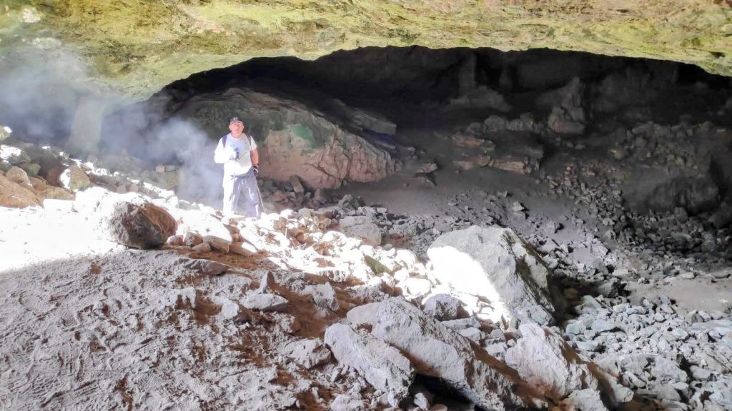 Interior de la Cueva dels Bous, mostrando un senderista de pie entre rocas, con luz natural iluminando la entrada.