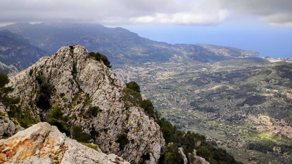 Font Es Verger-Portell de sa Costa-Caminando por Mallorca Vista panorámica desde el Morro de ses Solanes, mostrando valles y montañas en la distancia, con nubes cubriendo parcialmente el cielo.
