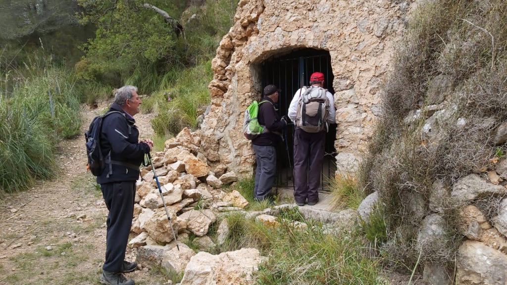 Tres personas observando la Font de sa Bastida en un entorno natural, rodeados de vegetación.