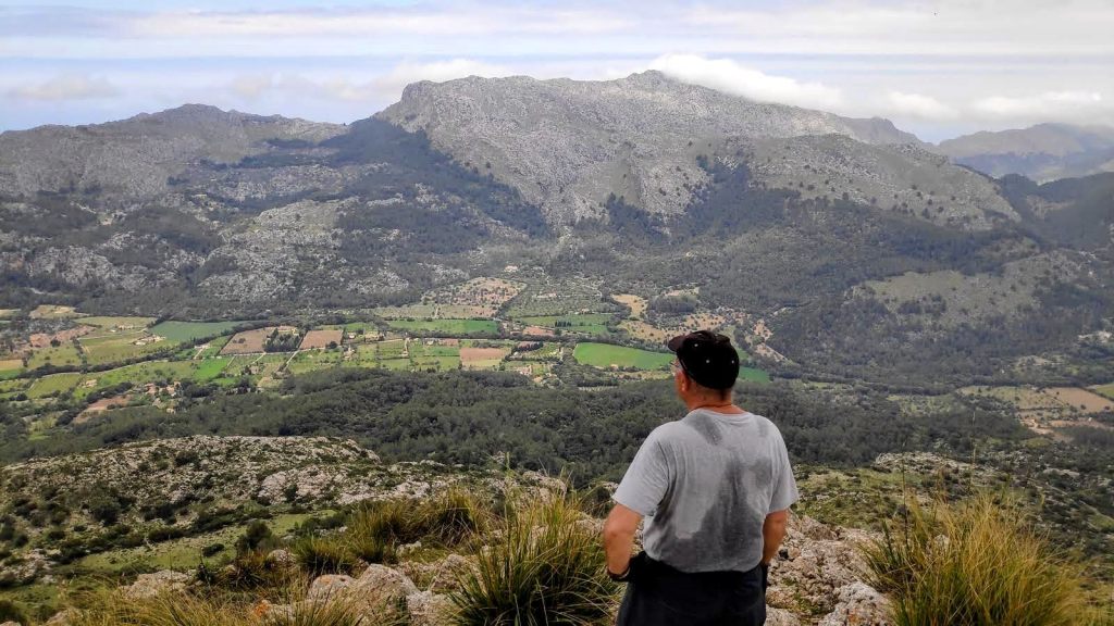 Hombre mirando hacia el paisaje montañoso con valles verdes y campos cultivados en la ruta Cuculla de Fartàritx.
