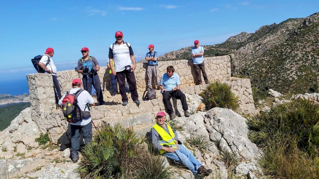 Grupo de excursionistas en la cima del Puig d'en Farineta, con vistas panorámicas y un mirador de piedra de fondo.