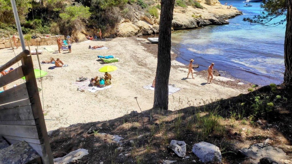 Playa de El Mago con bañistas y sombrillas, rodeada de rocas y vegetación en un día soleado.