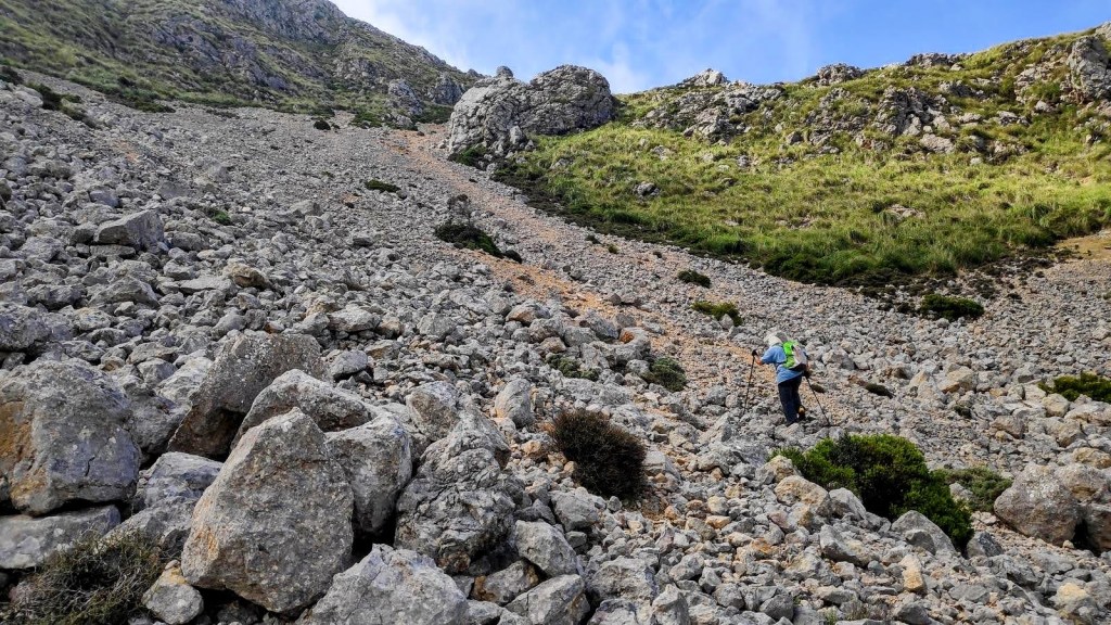 Puig Tomir, subida y circunvalación-Caminando por Mallorca Hombre ascendiendo por un terreno rocoso y accidentado en la ruta hacia Puig Tomir, rodeado de vegetación y montañas.