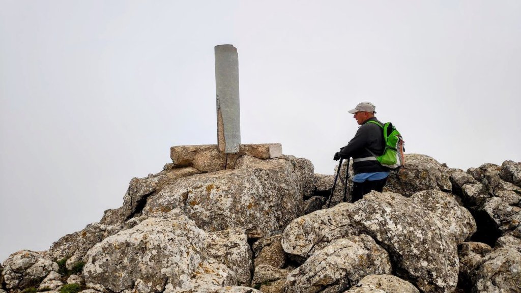 Puig Tomir, subida y circunvalación-Caminando por Mallorca Un senderista en la cima del Puig Tomir, rodeado de grandes rocas, con una estructura metálica en el centro.