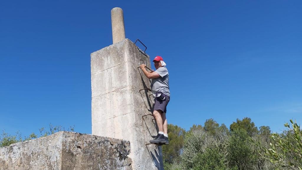 Hombre subiendo por una escalera de metal en un pilar de hormigón bajo un cielo azul.