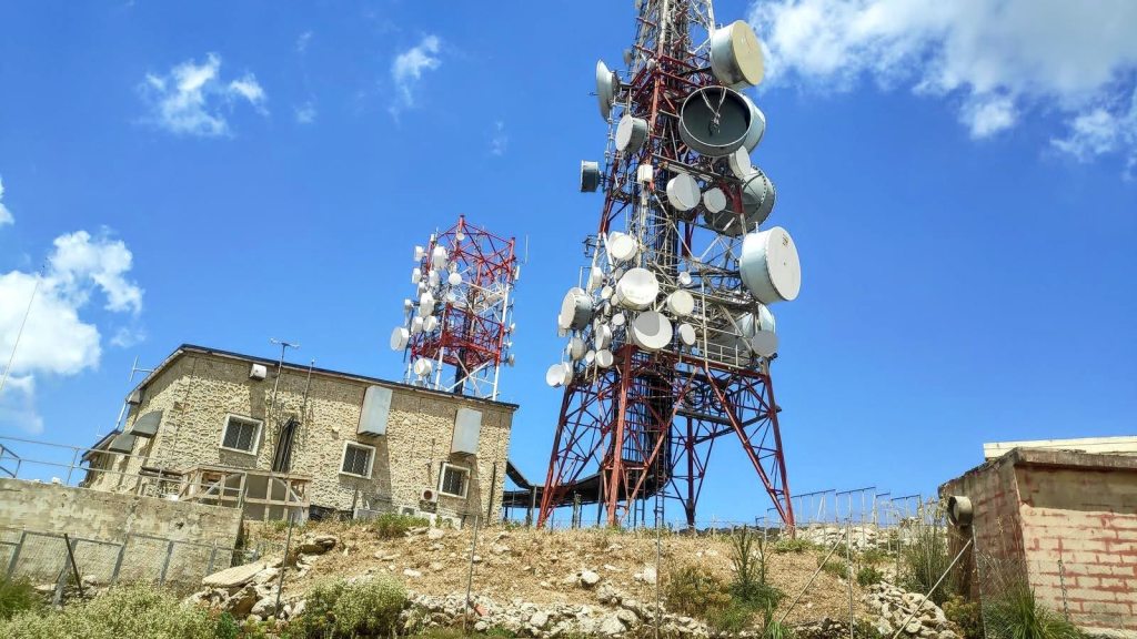 Antenas de telefonía y televisión en el Puig d'Alfàbia, con un cielo azul y nubes esponjosas.