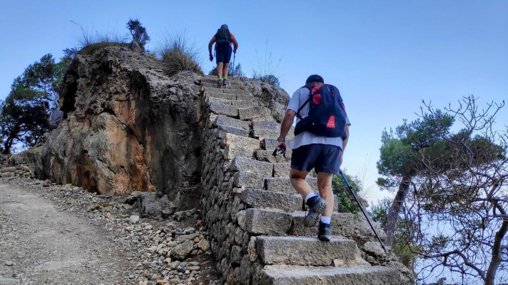Dos senderistas subiendo unas escaleras de piedra en una ruta de senderismo en la costa mallorquina.