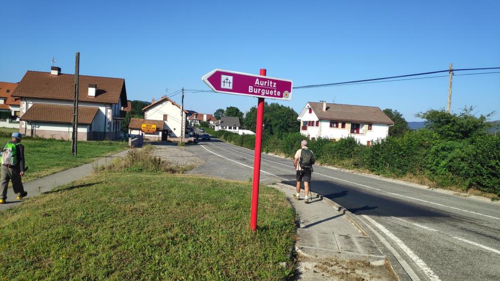 Señal de dirección hacia Auritz y Burguete, con un caminante en un sendero junto a la carretera en una zona rural.