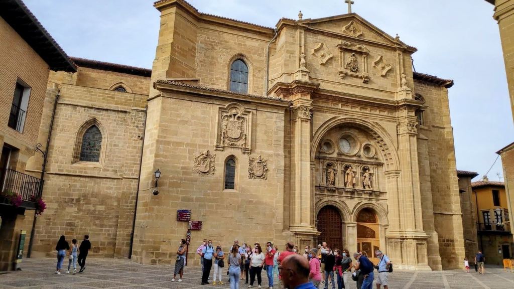 Vista de una iglesia histórica con una fachada elaborada y un grupo de personas en la plaza frente a ella.