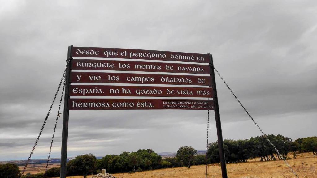 Etapa 12: Agés-Burgos. Caminando por Mallorca Una señal informativa del Camino de Santiago con texto en español, rodeada de campos y un cielo nublado.