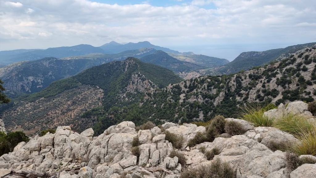 Vista panorámica desde el Puig de Sa Font, mostrando montañas y valles rodeados de vegetación, con nubes en el cielo.