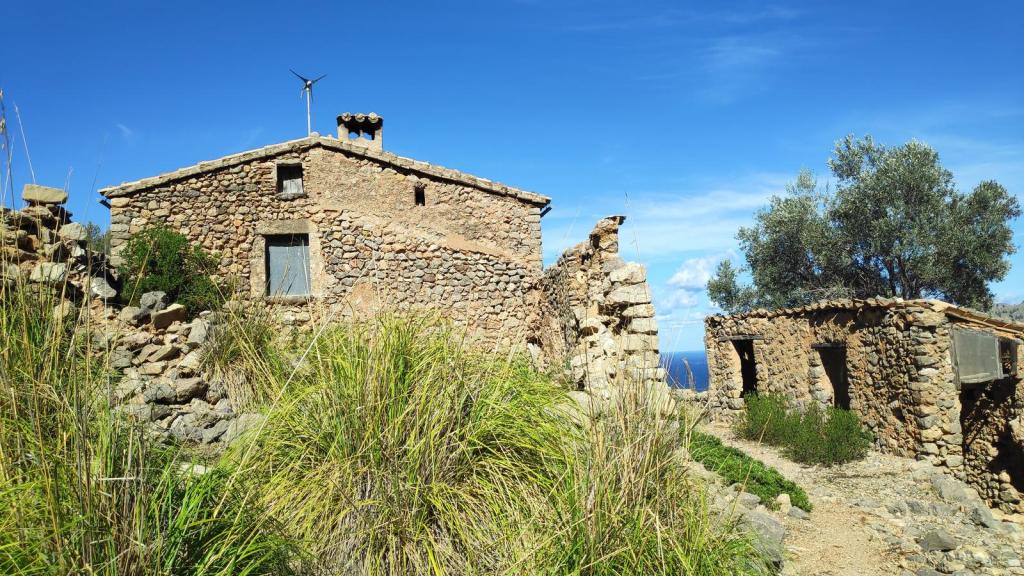 Vista de la Casa de Sa Costera, una construcción de piedra en un paisaje natural en Mallorca, rodeada de vegetación y con cielo azul de fondo.