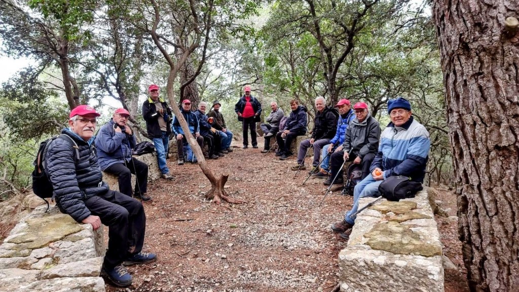 SES ERMITES VELLES-MIRADORES DE VALLDEMOSSA - Caminando por Mallorca Grupo de personas sentadas en un banco de piedra en un entorno boscoso, disfrutando de la naturaleza durante una excursión.