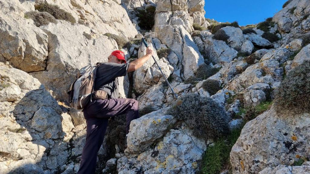 Una persona ascendiendo hacia la Mola de s'Esclop en la Ruta de la Pedra en Sec, utilizando un bastón de trekking y con una mochila.