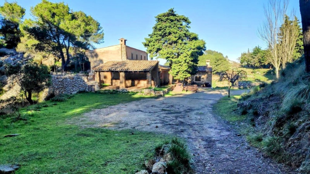 Vista del Refugio de la Coma d’en Vidal, rodeada de árboles y un camino de tierra.