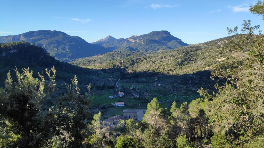 Vista panorámica de un valle rodeado de montañas, con vegetación abundante y pequeñas construcciones visibles en la llanura.