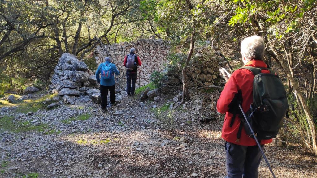 Tres personas caminando hacia un horno de cal en un entorno natural, rodeados de árboles y vegetación.