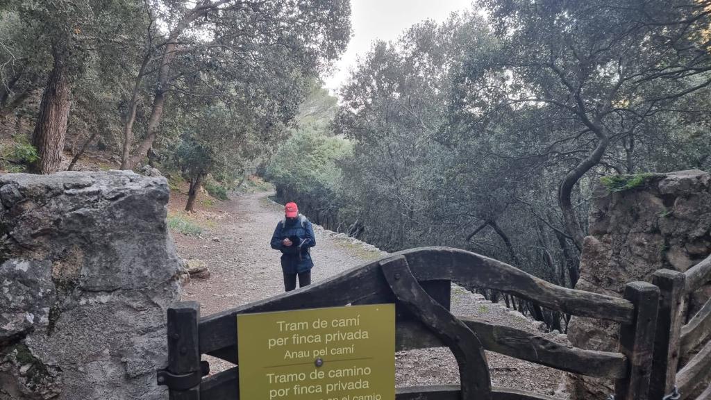 Una persona está de pie frente a una puerta de madera que da acceso a un sendero en un área boscosa, donde hay señales que indican que el tramo es para finca privada.