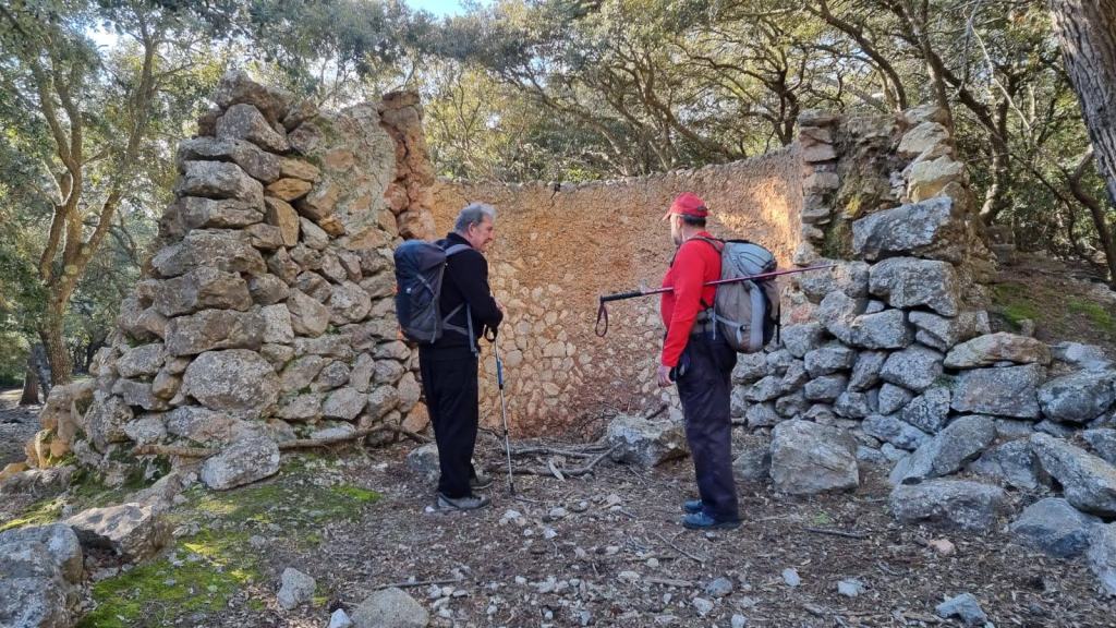 Dos personas de pie frente a un horno de cal  semi-destruido en un bosque, rodeados de árboles.