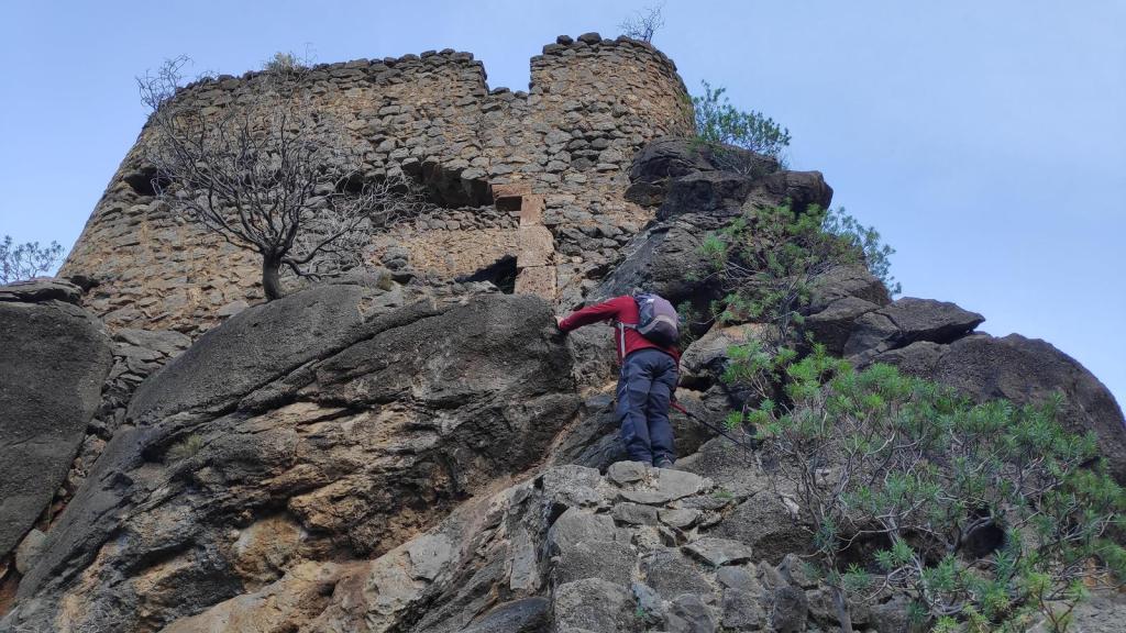 Hombre escalando un peñasco hacia una antigua fortificación del  Castell des Moro,.
