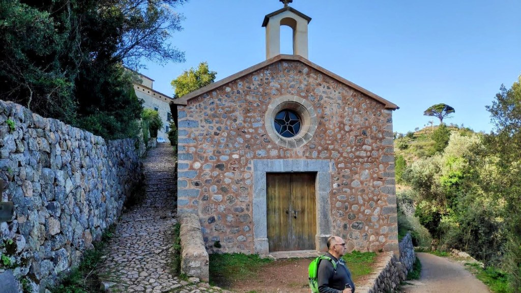 Vista de la capilla de Castelló en la Ruta de la Pedra en Sec, con un camino de piedra a su lado y vegetación alrededor.