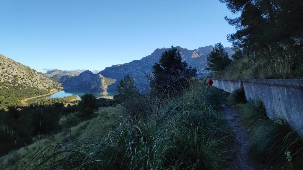 Vista panorámica de la Ruta de la Pedra en Sec-GR221-Etapa 8, con el embalse de Gorg Blau al fondo y sendero rodeado de vegetación y montañas.