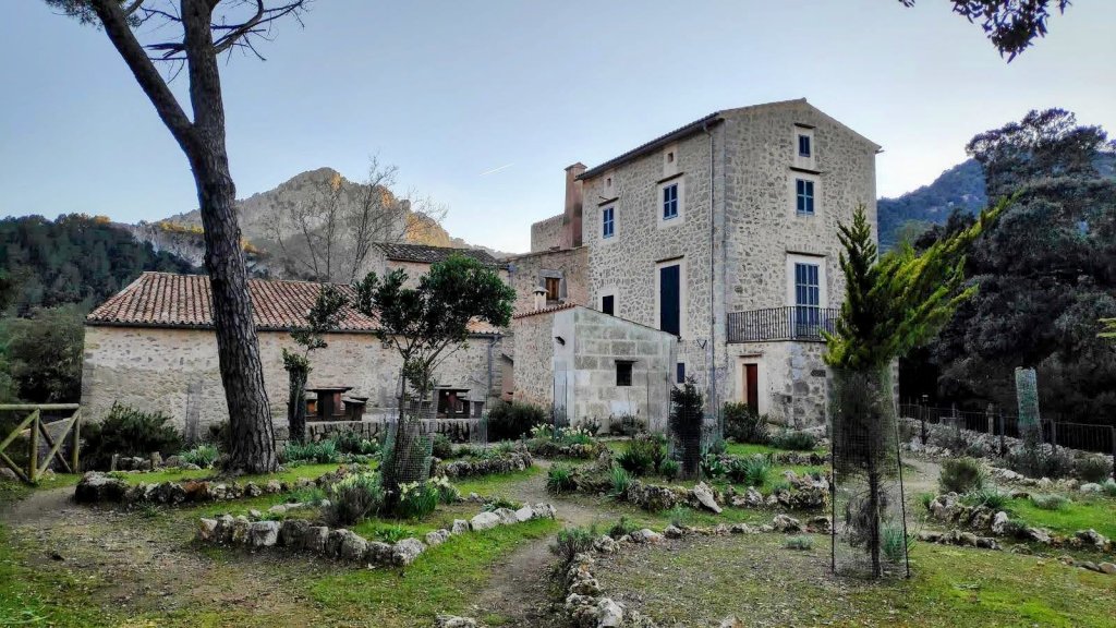 Refugio de Son Amer, rodeado de árboles y un jardín en primer plano, ubicado en las montañas de Mallorca.