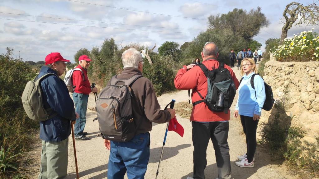 Grupo de excursionistas en un camino rural, conversando mientras disfrutan de la ruta 'María de la Salut y alrededores 4'.