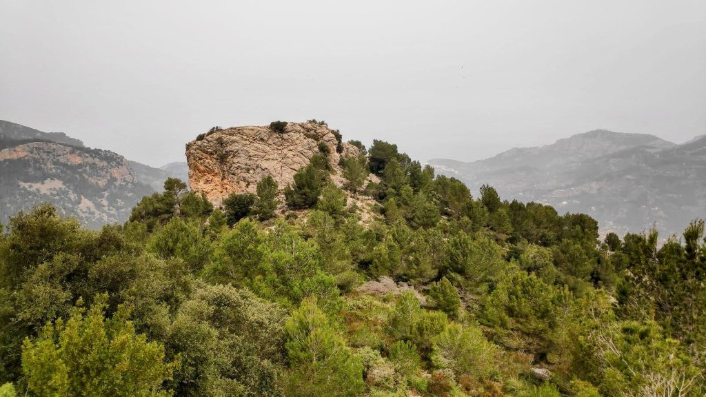 Vista de Es Castellot en medio de un paisaje montañoso con vegetación abundante, en un día nublado.