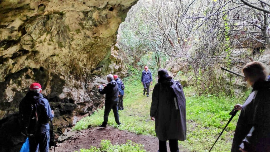 Grupo de personas explorando la Cova dels Coals, rodeados de vegetación y roca, en la ruta Finca de Son Quint.