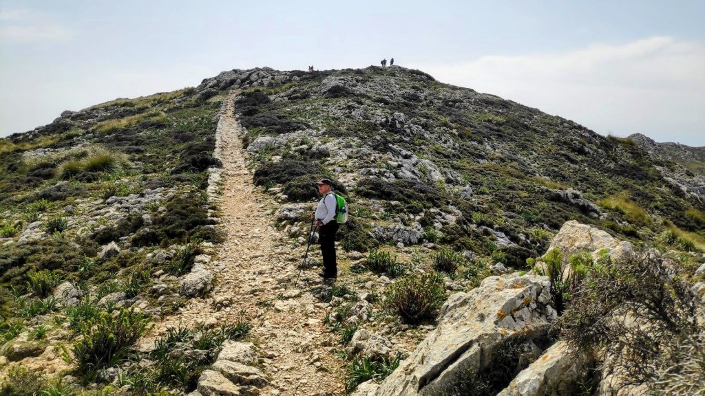 Camí de s’Arxiduc con un excursionista en primer plano, rodeado de paisaje rocoso y vegetación.