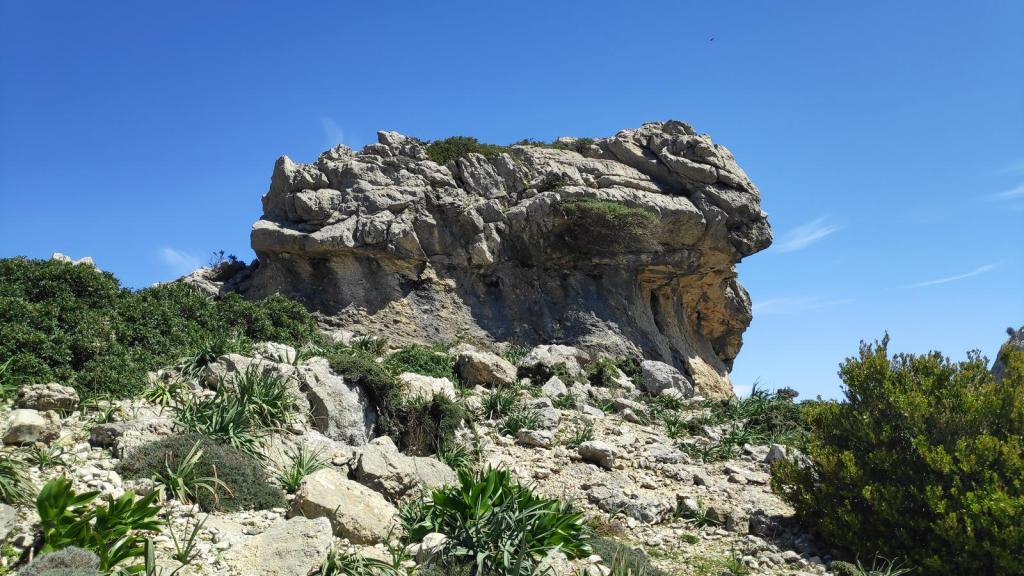 Puig Gros de Ternelles 2 - Caminando por Mallorca Formación rocosa conocida como 'El Paraigo' en la ruta Puig Gros de Ternelles, rodeada de vegetación y bajo un cielo azul.