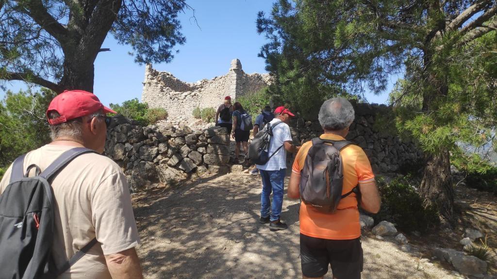 Grupo de personas caminando por un sendero hacia una antigua edificación en ruinas, rodeada de árboles en un ambiente natural.