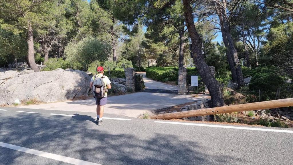 Senderista caminando hacia la entrada de la Finca de Moncaire, rodeado de vegetación y rocas, con un camino de cemento en la parte frontal.