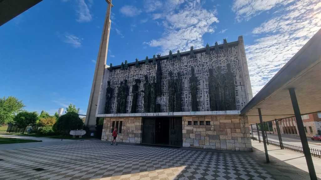 Fachada de la iglesia parroquial de Valverde de la Virgen en León, España, con un diseño moderno y estatuas prominentes, bajo un cielo azul con nubes.