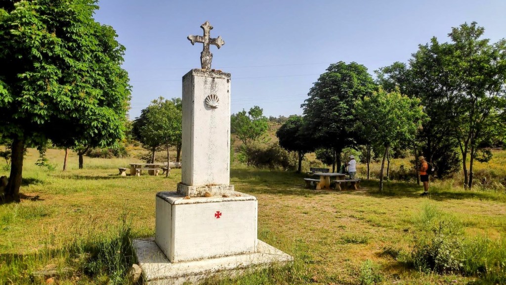 Cruz de Santiago en un área de descanso, rodeada de árboles y picnic, en la ruta del Camino de Santiago.