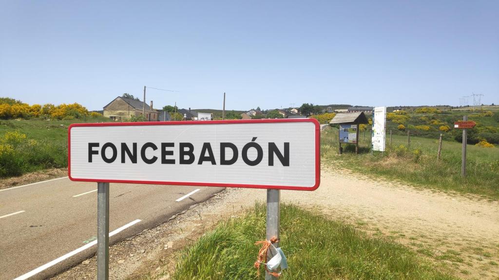 Señal de entrada al pueblo de Foncebadón con fondo natural de campos y algunas construcciones.